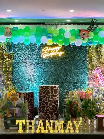 This jungle theme setup uses a sparkling green backdrop to create a forest feel. The decor is brought to life with a vibrant green balloon arch and large cutouts of a panda, bear, and elephant, personalized with the birthday boy's name in marquee letters.