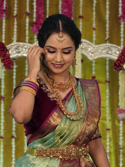 A candid shot of Harshitha adjusting her jewelry. The makeup is soft and photogenic, perfect for capturing these special moments.