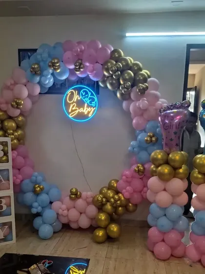An "Oh Baby" gender reveal decoration with a circular balloon arch. The arch is decorated with pink, blue, and gold balloons, with matching balloon pillars and "BABY" blocks.