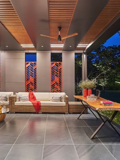 This covered outdoor patio is designed for comfort and style. It features modern wicker furniture, a rustic wooden table, and decorative panels with a chevron pattern, creating an ideal space for alfresco dining and lounging.