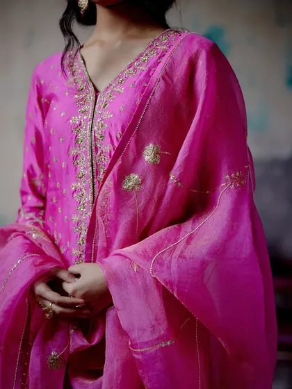 A close-up of a fuchsia sharara set, highlighting the intricate handwork around the neckline. The bold colour and delicate embroidery make this a standout piece for any celebration.