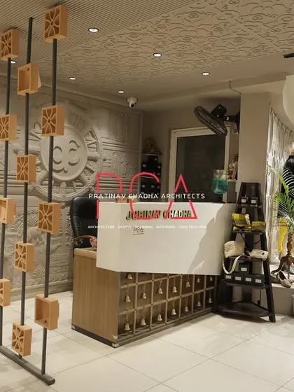 The reception area of the fashion studio features a custom-designed desk and a decorative screen made of wooden blocks. Behind the desk, a large, stone-carved mural adds a significant touch of traditional artistry.