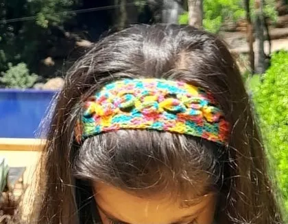 A look at my handmade crochet headband, designed with a multi-color yarn and a pattern of small, raised flowers. It's a comfortable and stylish hair accessory for both children and adults.