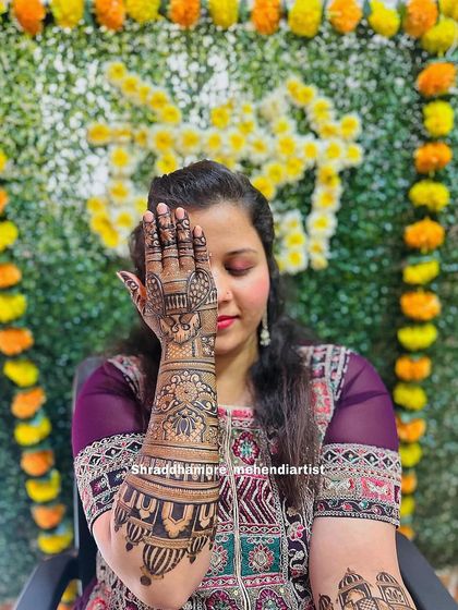 A classic mehendi pose, with the bride covering one eye to showcase the detailed design on her hand and arm.