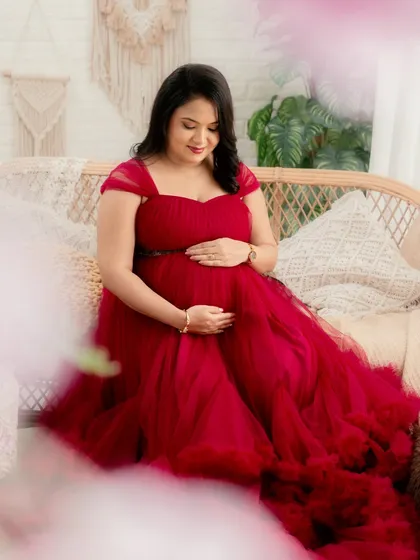 A quiet moment of connection. This portrait captures the mom-to-be looking down at her bump, framed by soft, dreamy elements in a beautiful red gown.
