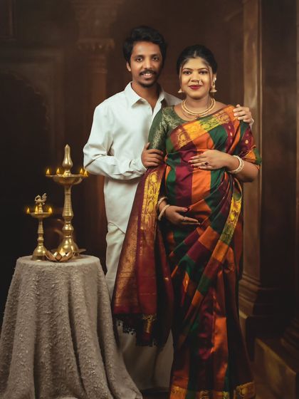 A classic couple's portrait, with the partners dressed in beautiful traditional attire, standing by ornate brass lamps.