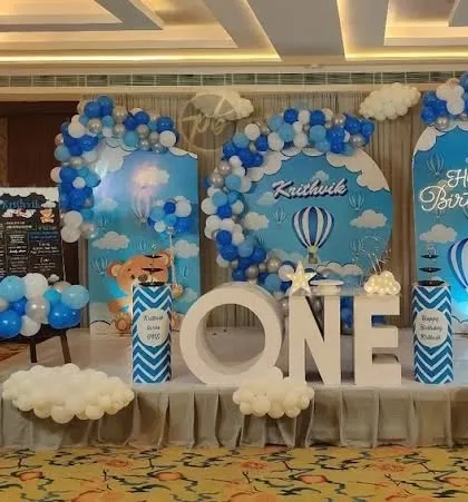 A sky theme party with hot air balloons and a cute teddy bear. The setup uses multiple backdrops and balloon clouds to create a sense of height and wonder.