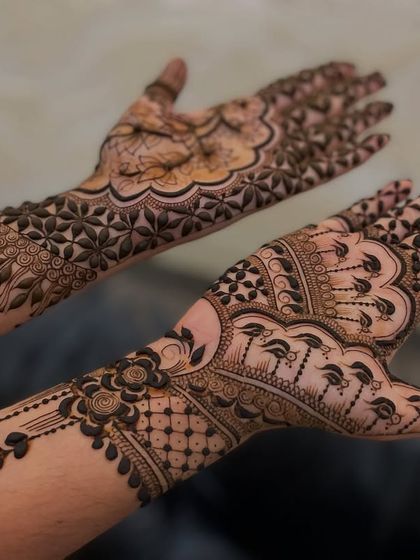 A beautiful example of asymmetrical mehandi, where each hand has a different but complementary design. One hand has a floral net, while the other has a more traditional pattern.