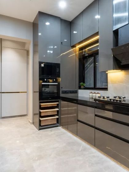 A wider view of our open kitchen concept, showing the seamless integration with the living area. The charcoal grey cabinetry and high-rise island counter create a bold yet refined presence, exemplifying modern luxury.