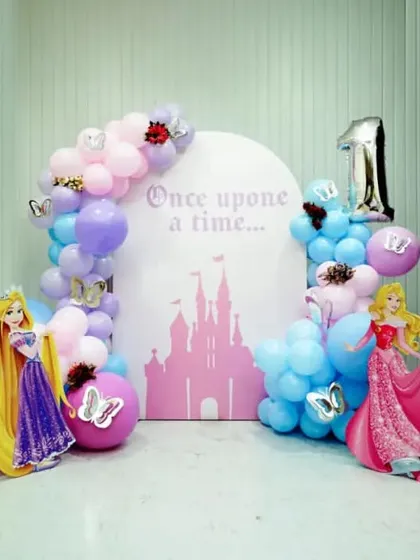 A classic Disney Princess first birthday party. This setup includes life-sized cutouts of Ariel, Rapunzel, Aurora, and Snow White against a castle-themed backdrop.