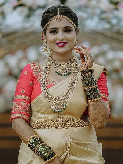 A classic bridal portrait showcasing the full wedding attire against a beautiful floral arch. I make sure to capture the bride's complete look, highlighting the elegance of the saree, the intricate temple jewellery, and the confident smile.