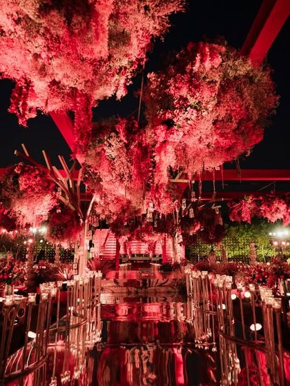 A stunning overview of the all-red mandap and dining setup. The mirrored aisle reflects the dramatic floral canopy and candlelight, doubling the impact and creating an immersive experience of royalty and romance for every guest.