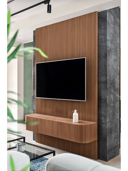 This floating TV unit is a statement piece, crafted with a wooden fluted panel that curves at the bottom. Set against a dark, textured wall, it creates a sophisticated and modern focal point in the living area.