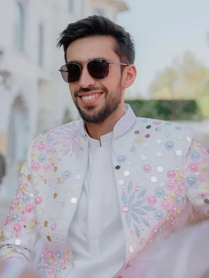 A close-up of the groom's custom-designed jacket. The white base is brought to life with pastel-colored floral embroidery and sequins, creating a look that is both celebratory and sophisticated.
