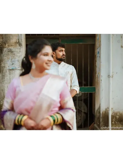 An artistic shot using depth of field to create a story. The bride is in soft focus in the foreground while the groom looks on from the background, suggesting a moment of quiet anticipation.
