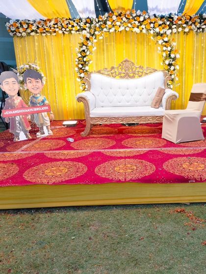 A close-up of the Haldi stage with personalized couple caricatures. The white and gold sofa provides elegant seating for the bride and groom.
