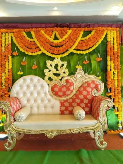 A baby shower stage featuring a backdrop of banana leaves and marigold garlands. The ornate sofa provides a comfortable and royal seating area for the mother-to-be.