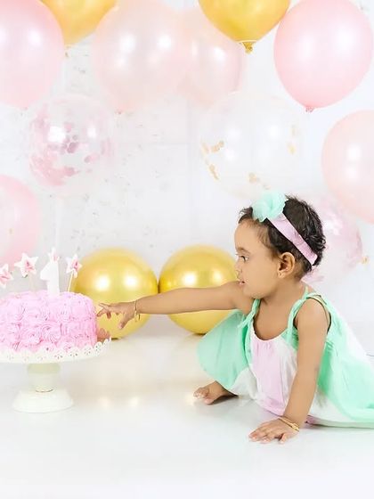 A baby girl curiously reaches out to touch the candle on her first birthday cake. A sweet moment of discovery.