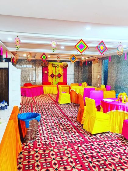 A wide view of an indoor hall decorated for a Mehendi function, showing the main stage, guest tables, and buffet area.