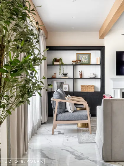 Faux ceiling beams add a touch of traditional charm, contrasting with the clean lines of the contemporary furniture. An olive tree brings a touch of nature indoors, softening the space.
