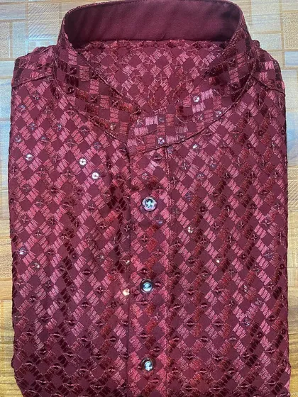 A folded view of a festive men's kurta in a rich maroon, made from a patterned fabric with delicate sequin work. This piece highlights the kind of detailed craftsmanship available for special occasions like Diwali or sangeet ceremonies.