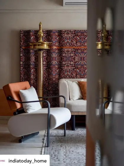 A view of the living room, where a modern white armchair is placed next to a traditional brass diya and a custom Kalamkari fabric art piece. It's a beautiful fusion of old and new.