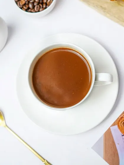 A flatlay of a coffee cup, styled with a golden spoon and aesthetic postcards. This type of image is trendy and performs well on social media for cafes and lifestyle brands.