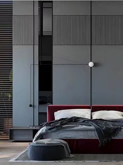 A dramatic and masculine bedroom design combining a deep red accent wall with dark grey paneling. The leather armchair and minimalist furniture create a sophisticated and modern space.