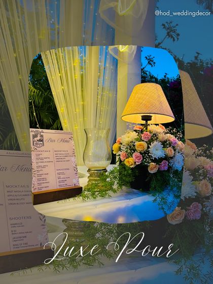 A "Luxe Pour" bar corner, with a cozy table lamp, a custom menu, and floral arrangements creating an intimate and sophisticated spot for drinks.