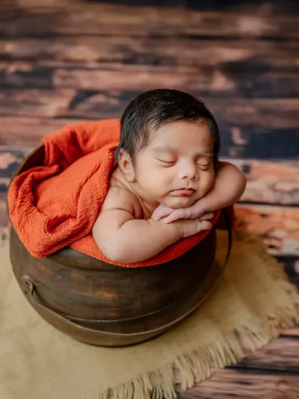 This classic 'pot pose' is perfect for showing off a baby's adorable chubby cheeks and arms. The warm orange wrap complements the rustic wooden background.