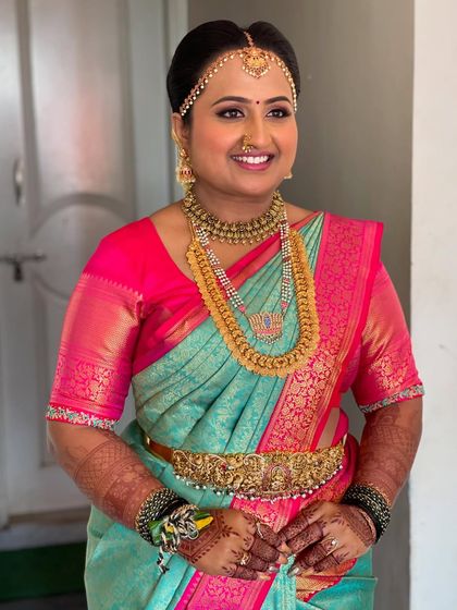 Bride Supritha looking radiant in her vibrant Muhurtham saree. Her makeup features a subtle pink eyeshadow to match her blouse and a warm, glowing complexion, making her look absolutely ethereal.