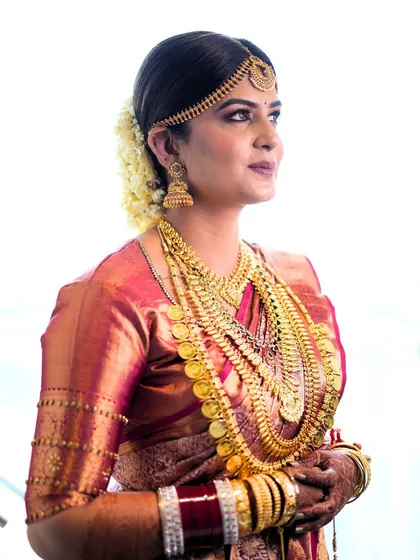A classic portrait of the South Indian bride. Her makeup is timeless, with a focus on clean lines and a radiant finish that complements her elaborate gold jewelry.