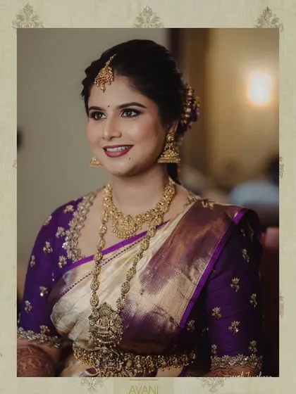A bride in a cream and purple Kanchipuram saree. Her custom purple blouse is adorned with delicate gold embroidery, perfectly matching her temple jewelry.