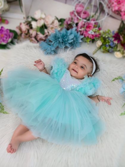 An angel on a cloud. This sweet baby girl in her light blue dress looks ethereal lying on a soft, fluffy rug surrounded by flowers.