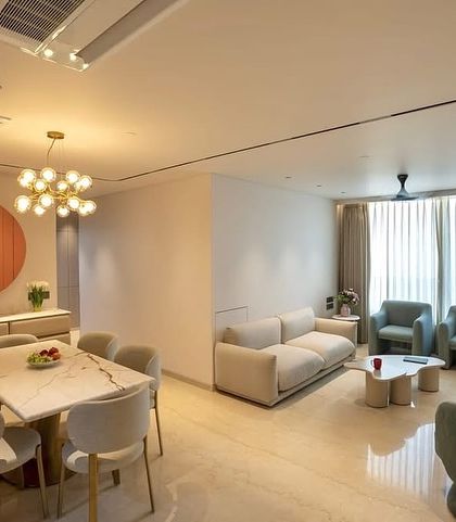 A wider view of the Oberoi Sky City apartment, showing the open-plan living and dining area. The design maintains a cohesive and sophisticated palette of beige and soft blues, unified by modern lighting and clean lines.
