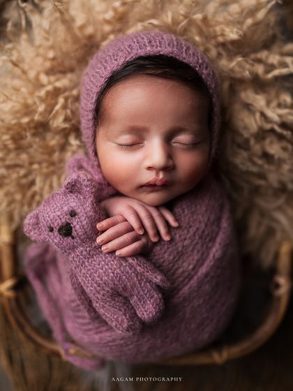 A closer view of the baby and their teddy, showcasing the rich textures of the purple wrap and the fluffy wool below.