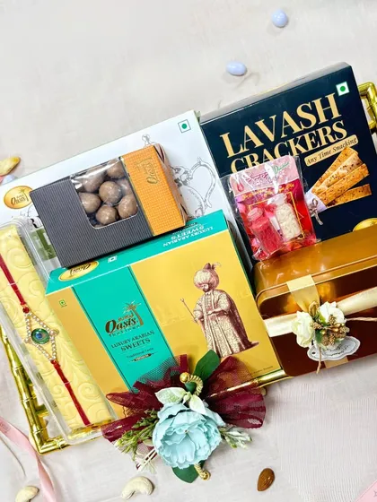 This Rakhi hamper, set in a golden bamboo-style tray, offers a luxurious mix of Lavash crackers, assorted sweets, and chocolate balls, all beautifully arranged.