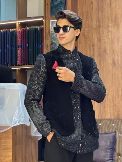 A client looking dapper in a black sequined Indo-Western outfit with a velvet jacket. The pocket square adds a pop of color to the monochrome look.
