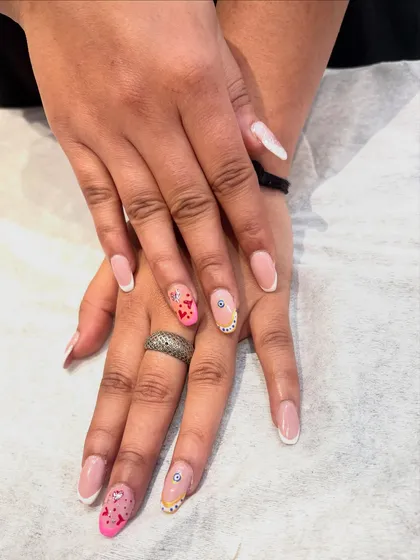 Your nails deserve to tell a story. This custom set features classic French tips alongside accent nails with pink hearts, glitter, and a tiny evil eye charm for good vibes.