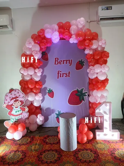 A sweet "Berry First" birthday theme featuring Strawberry Shortcake. The decor uses a red and pink balloon arch and a character cutout to create a cute and memorable first birthday setup.