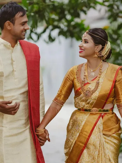 A happy couple shot. The bride wears a gold and red Kanchipuram saree with a custom blouse, looking radiant on her wedding day.