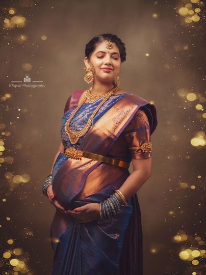 A fine art maternity photoshoot featuring a mother-to-be in a traditional blue and gold silk saree, glowing with anticipation.