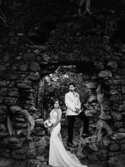 A dramatic black and white version of the editorial portrait in the stone arch. The monochrome treatment enhances the texture of the rocks and the moody atmosphere.