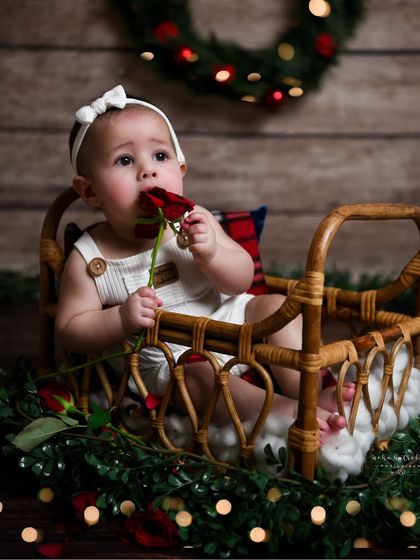 Another variation from the festive session, this time in a cute outfit and a rattan bed prop. The baby curiously nibbling on a rose adds a touch of spontaneous charm.