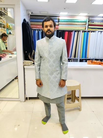 A client wearing a light grey sherwani with self-embroidery, paired with a grey kurta. This monochromatic look is modern and sophisticated.