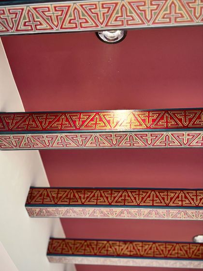 The finished hand-painted rafters installed on a deep red ceiling. The intricate geometric patterns add a layer of tradition and poetic detail to the room's architecture.