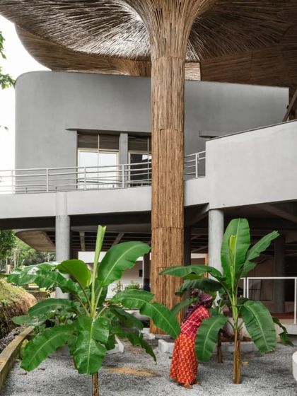 A view showing the relationship between the bamboo-clad columns and the surrounding greenery at the TAPMI Centre. The architectural elements are designed to mimic and blend with the natural forms of the landscape.