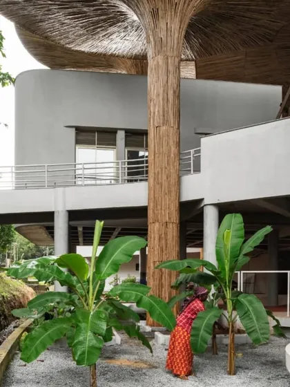 A view showing the relationship between the bamboo-clad columns and the surrounding greenery at the TAPMI Centre. The architectural elements are designed to mimic and blend with the natural forms of the landscape.