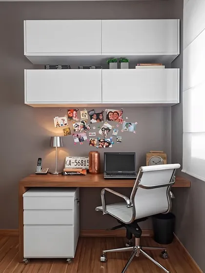 A clean and simple home office corner. The design features a wooden desk, a mobile drawer unit for flexible storage, and white floating cabinets overhead, creating a practical and uncluttered workspace.