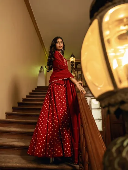 A dramatic, low-angle shot on a grand staircase, making the model in her red polka-dot lehenga look powerful and statuesque. The warm lantern light adds to the vintage, cinematic feel.